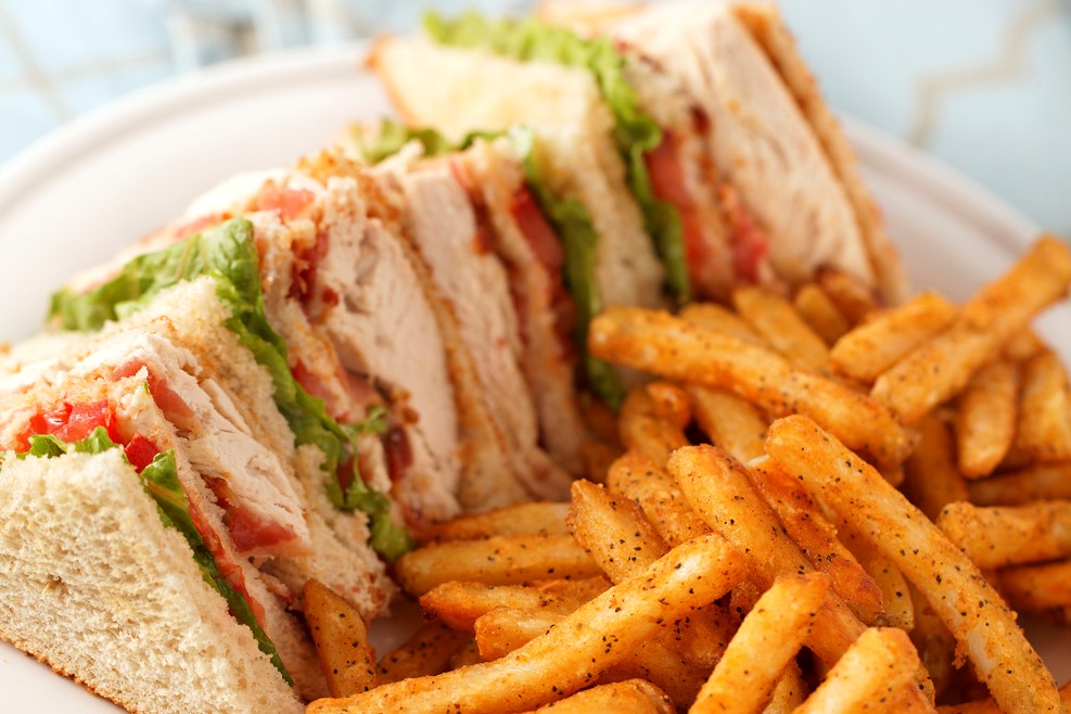 chicken club sandwich on a white plate with spicy french fries. Very Shallow depth of field.