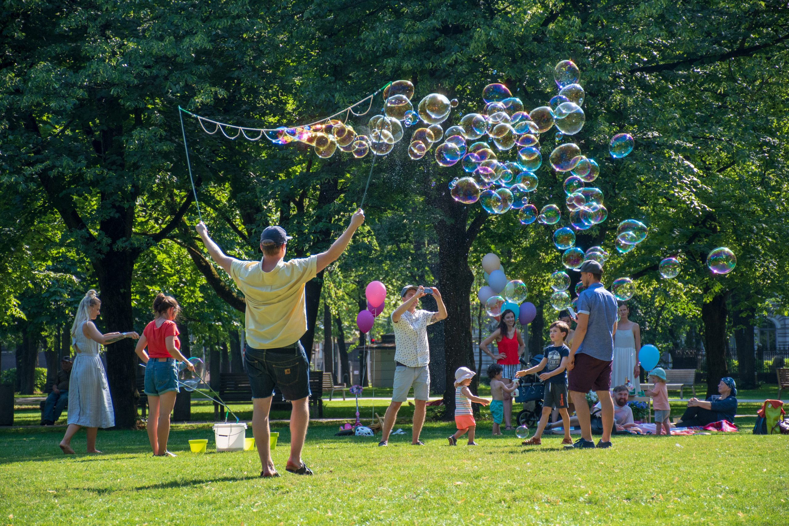 Riga / Latvia - Juy 27 2019: Children play outdoors in a park with their parents on a sunny day, with soap bubbles
