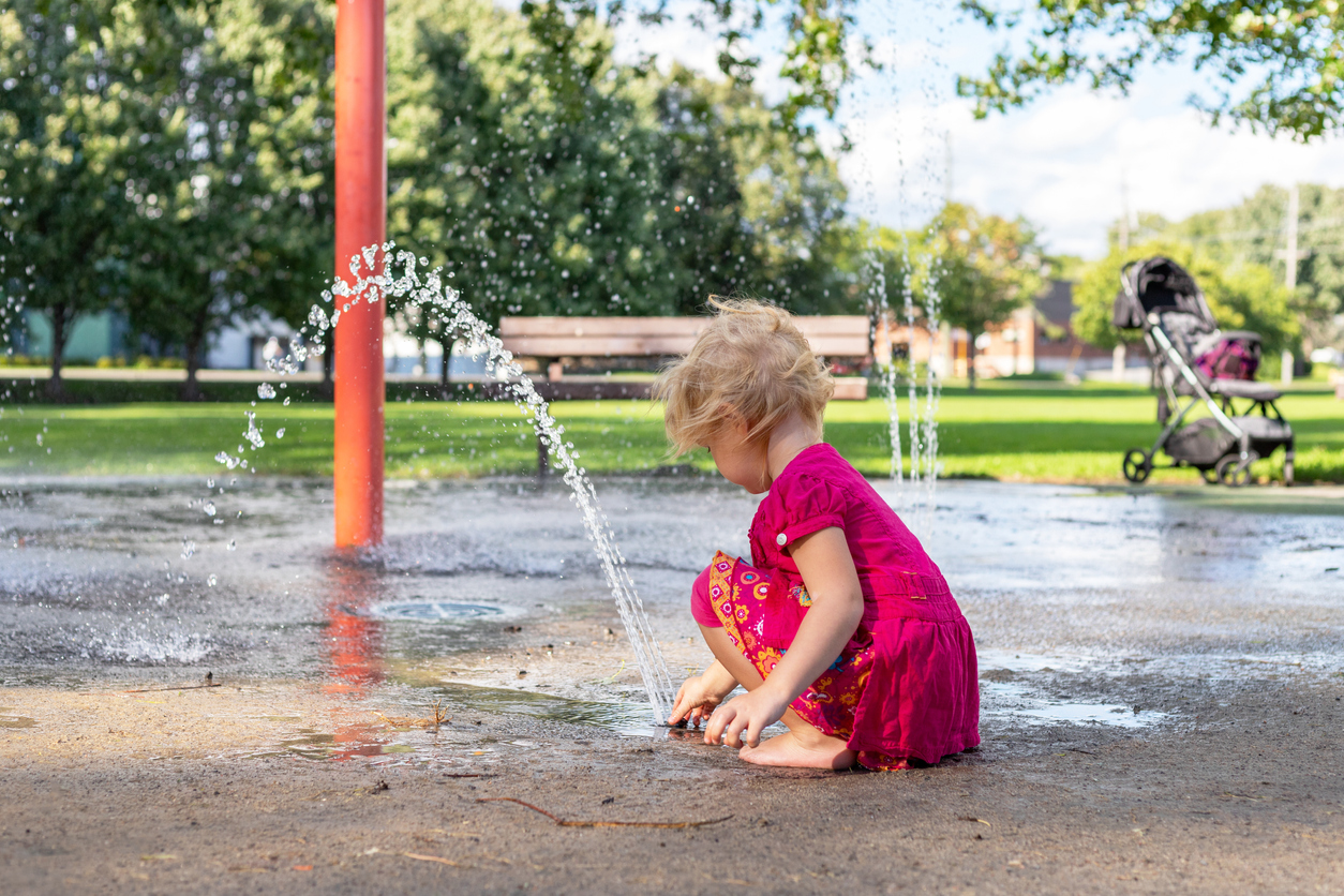 Little girl playing with splash pad water and dirt in the park on sunny day in summer.